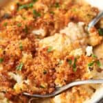 Cheesy cauliflower casserole in a white dish with spoons.