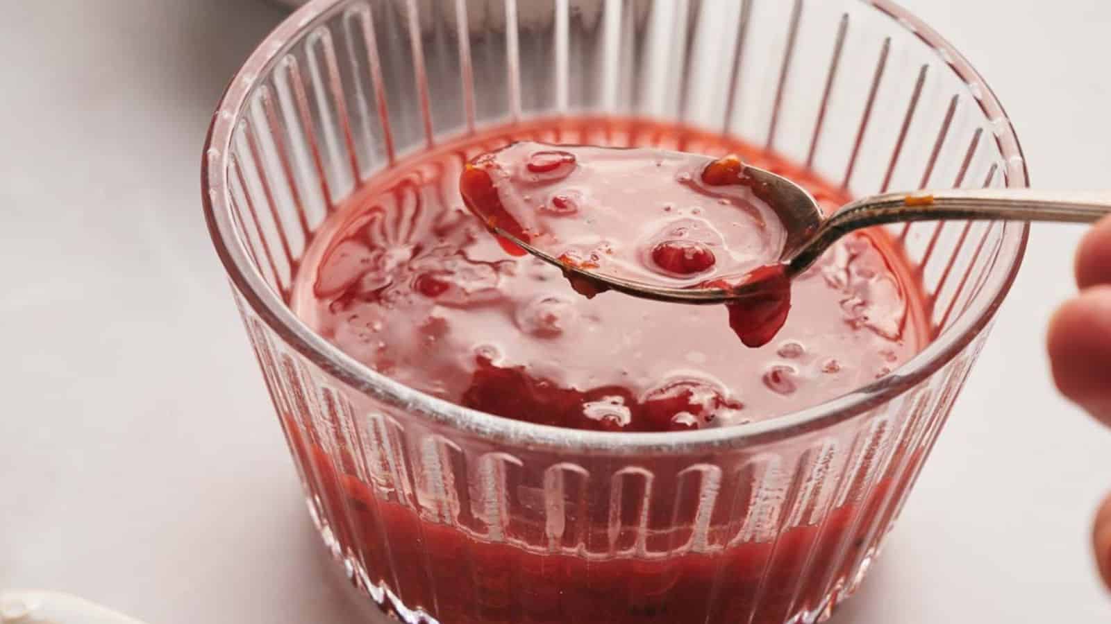 Someone spooning out cranberry sauce from a glass bowl.