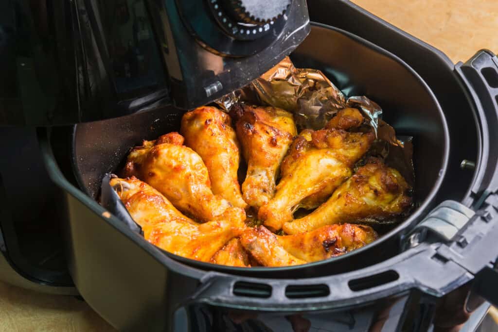 An air fryer with chicken wings on top of aluminum foil.