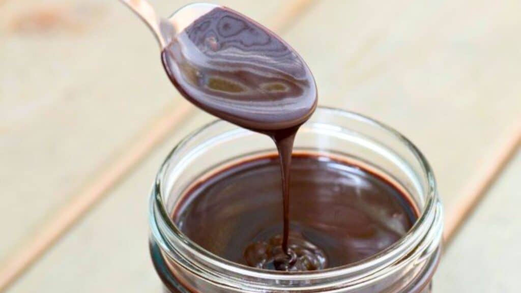 Image shows A spoon is pouring espresso hot fudge sauce into a jar.