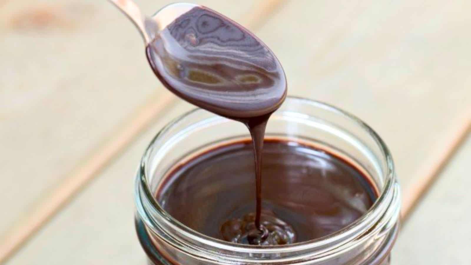Image shows  A spoon is pouring espresso hot fudge sauce into a jar.