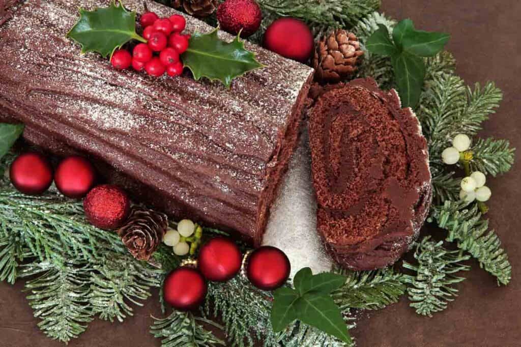A chocolate log cake with berries and leaves.