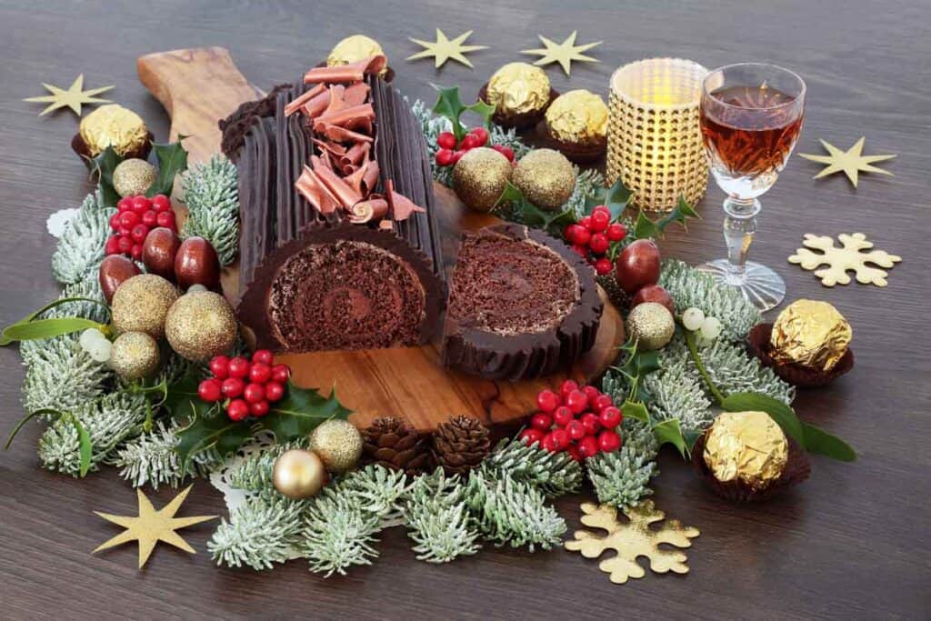 A chocolate log cake with a glass of wine and decorations.