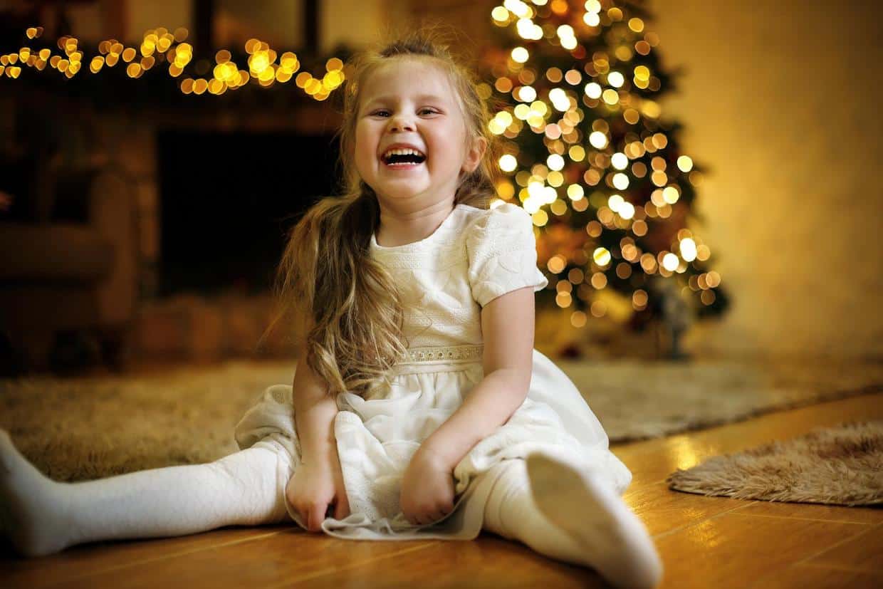 A little girl sitting on the floor in front of a christmas tree lauging.