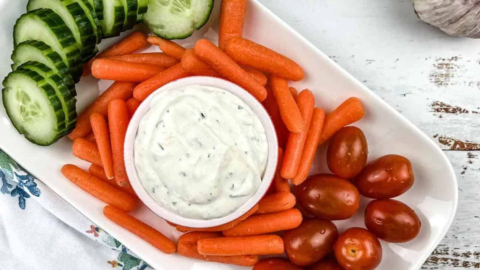 A plate with carrots, cucumbers and garlic dip.