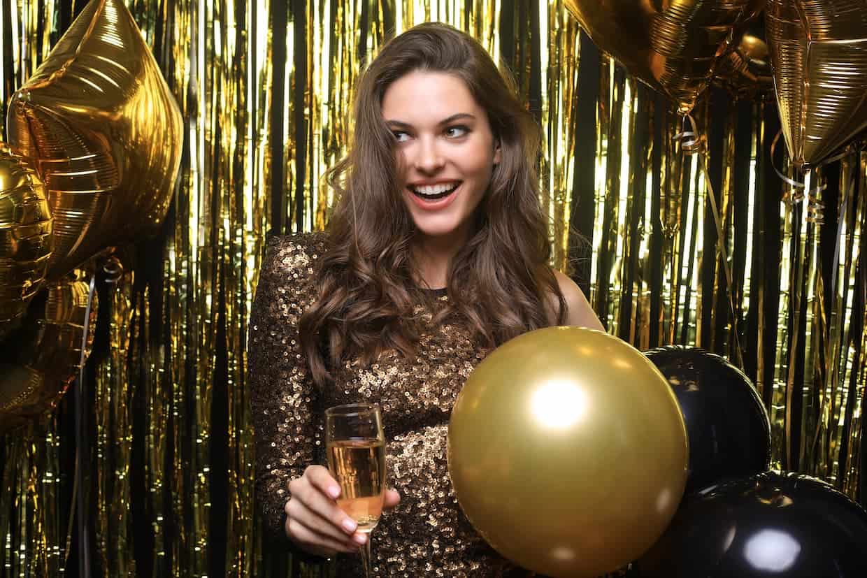 A woman holding a champagne flute and gold balloons at a gold themed Christmas party.