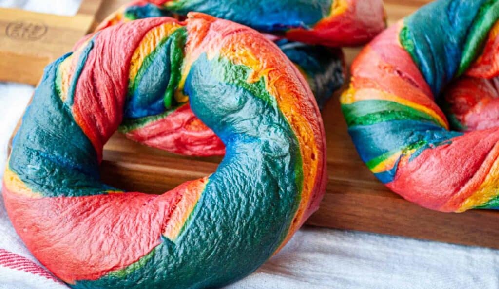 A rainbow colored bagels on a wooden surface.