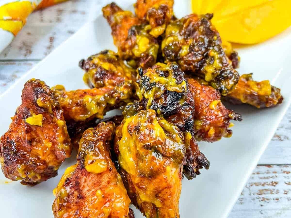 A plate of chicken wings on a white plate with a slice of mango.