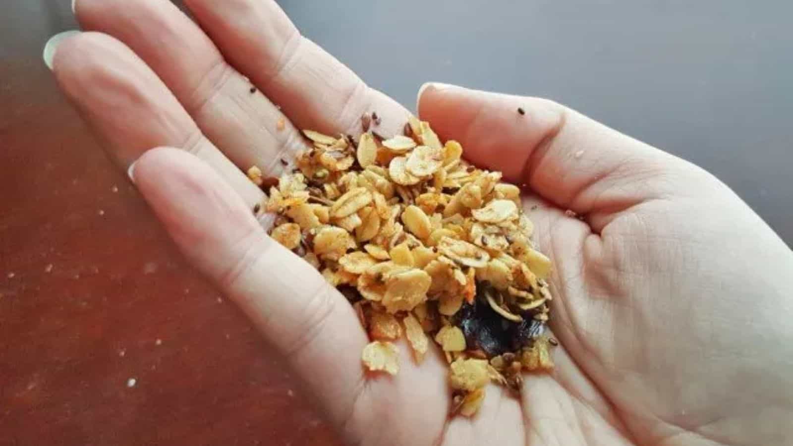 Image shows  A person holding a handful of granola in their hand.