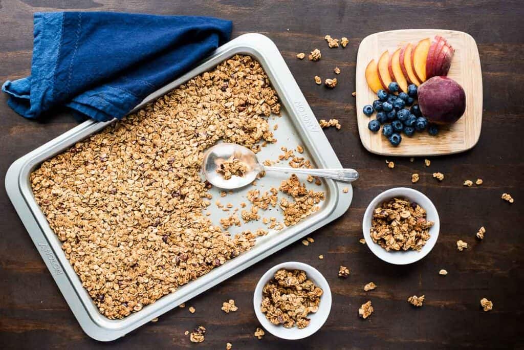 Granola on a tray next to servings of granola and fresh fruit.