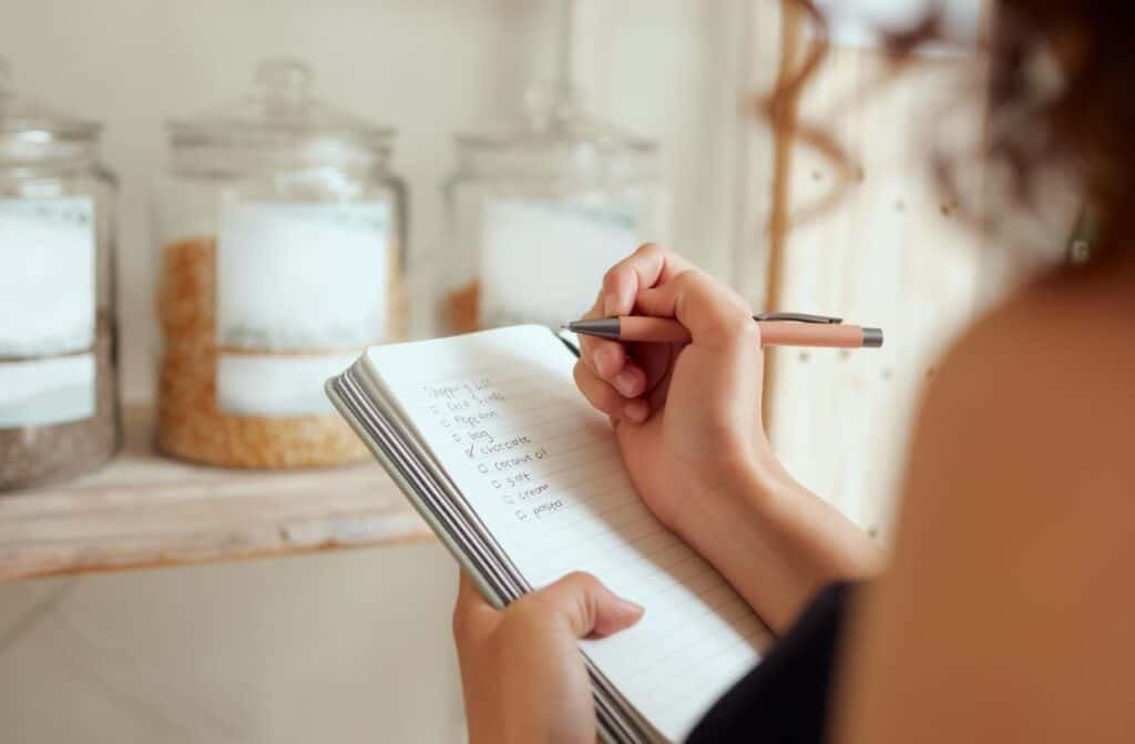A woman meal planning in a notebook next to jars of food.