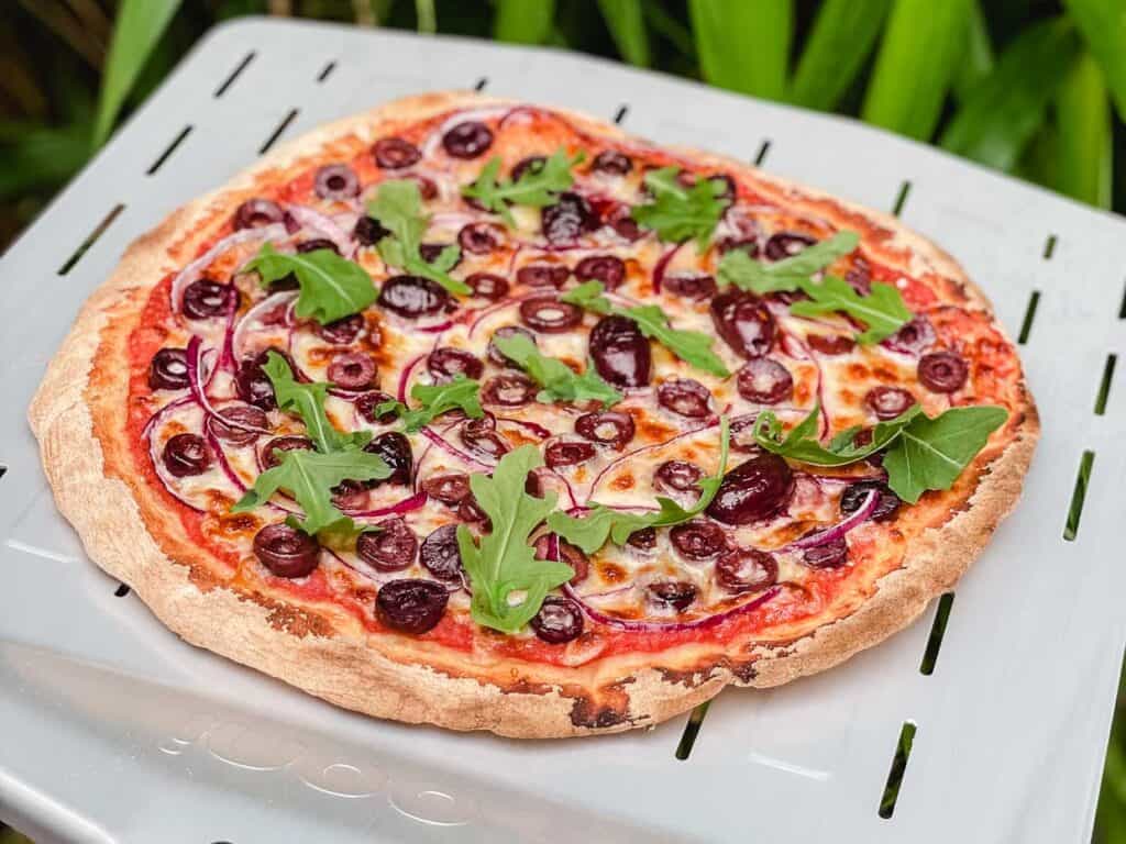 A pizza with olives and greens on top.