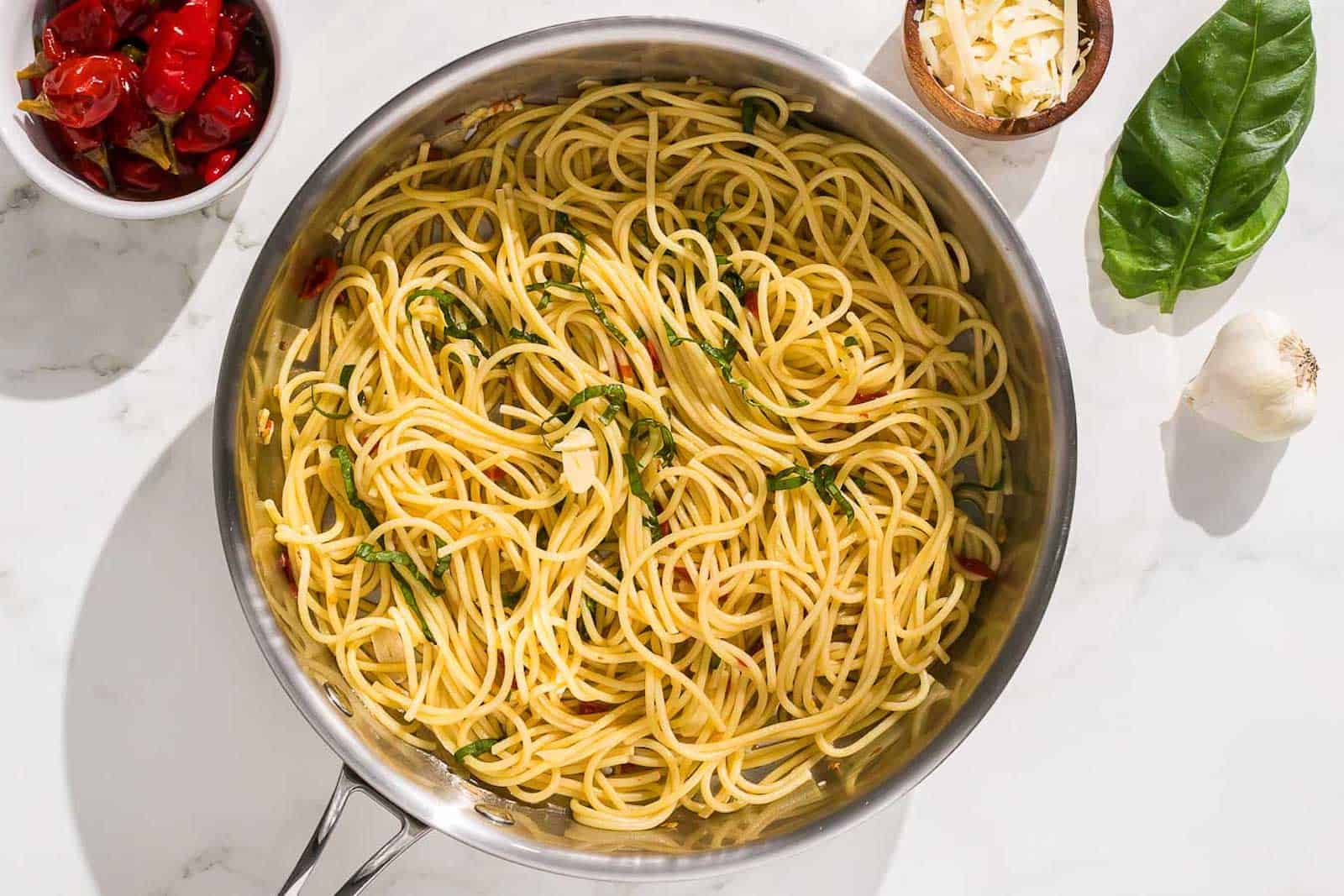A pan of spaghetti with basil, chilis, and garlic.
