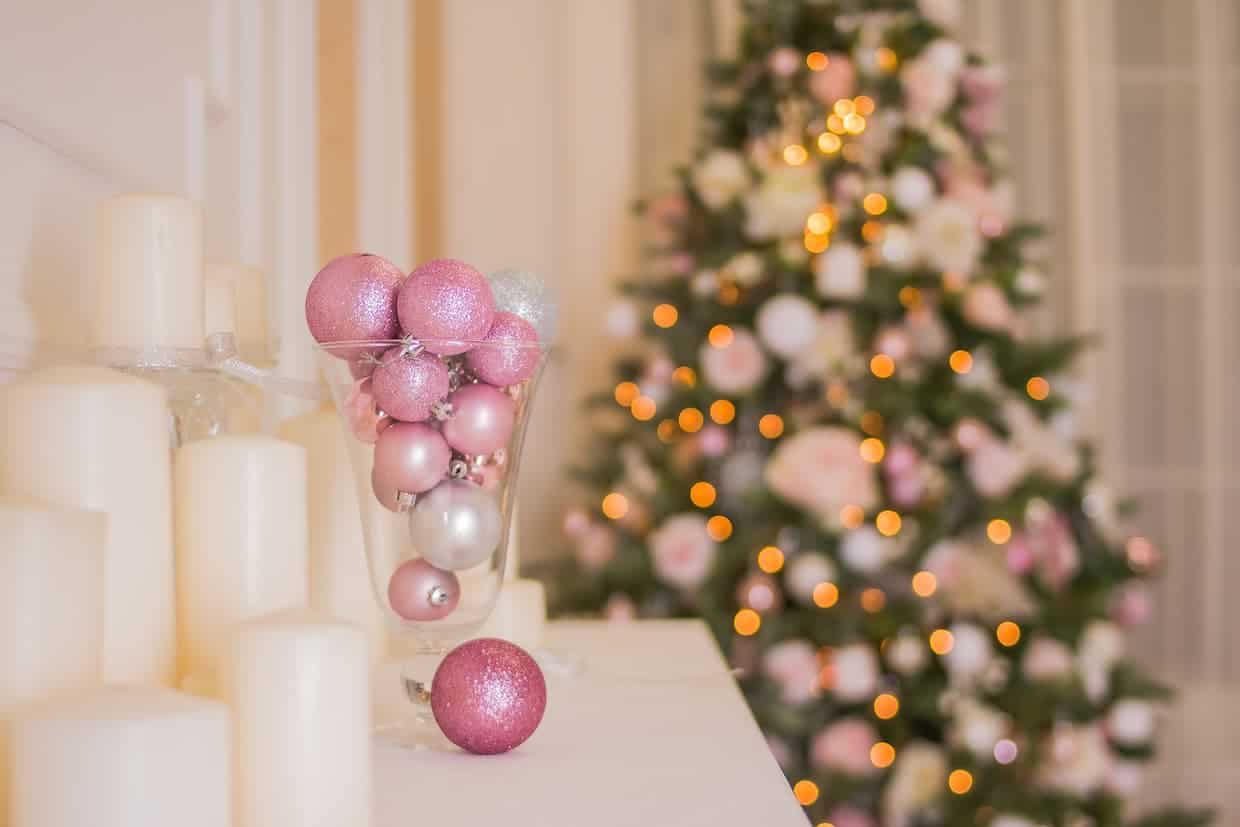 A christmas tree with pink ornaments and white candles in front of it.
