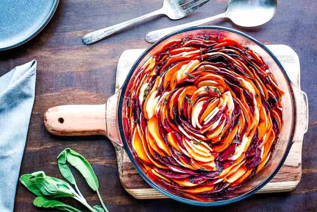 A dish of beets, sweet potatoes, and parsnips roasted in the oven with sprigs of sage.