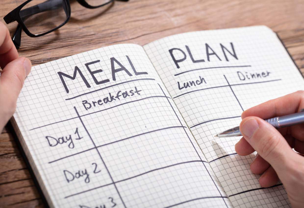 A person writing a meal plan in a notebook.