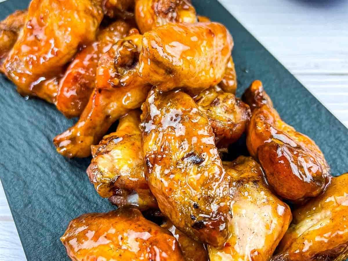 Smoked and glazed peach-chipotle chicken wings on a black plate.