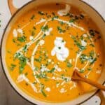 A bowl of sweet potato and red pepper soup with sour cream and parsley.