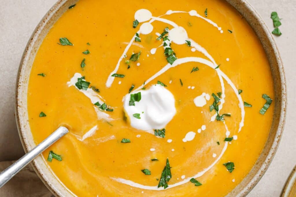 A bowl of sweet potato and red pepper soup with sour cream and parsley.