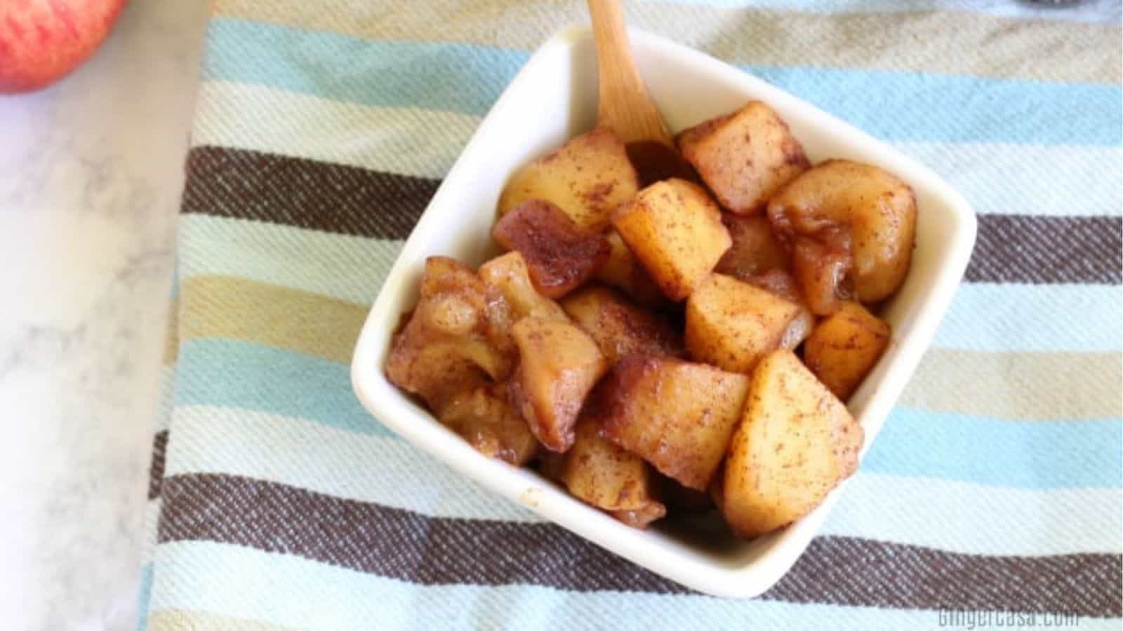 White bowl of cinnamon apples with a spoon.