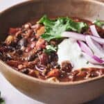 Two bowls of chili with onions and sour cream.