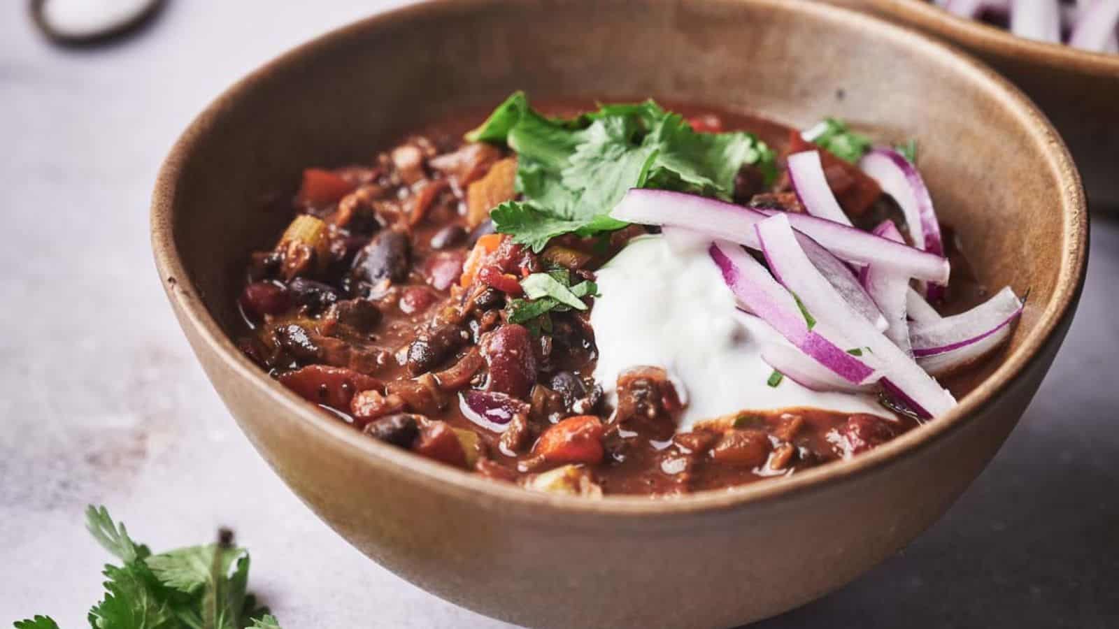 Two bowls of chili with onions and sour cream.
