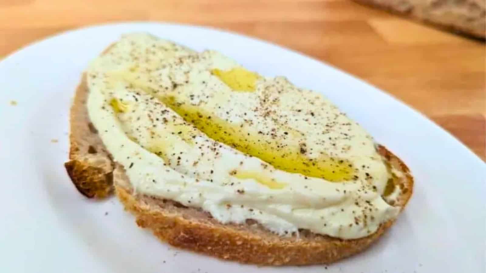 Image shows a white plate with whipped ricotta toast drizzled with olive oil on it.