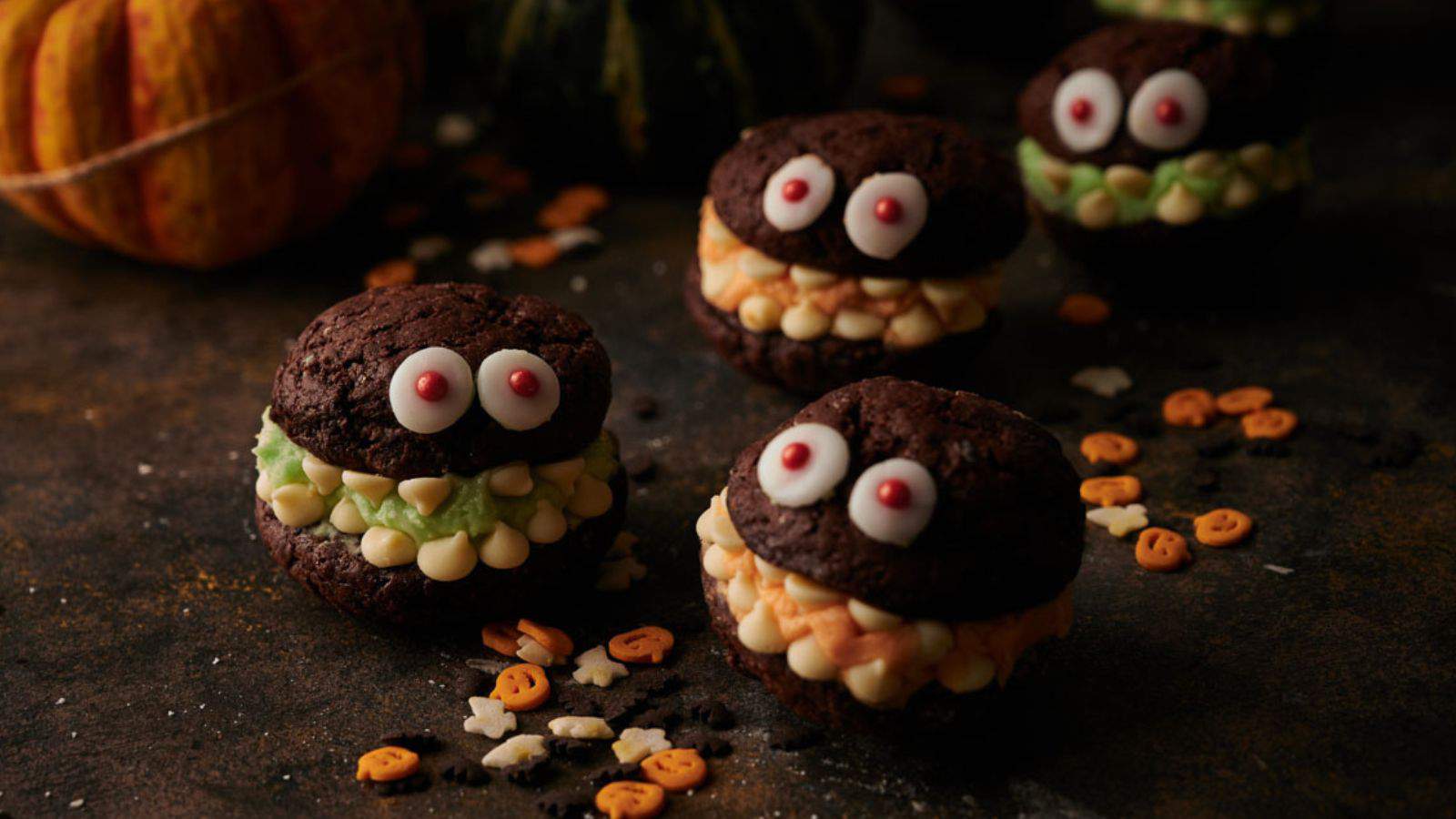 A group of chocolate monster cookies on a table with pumpkins.
