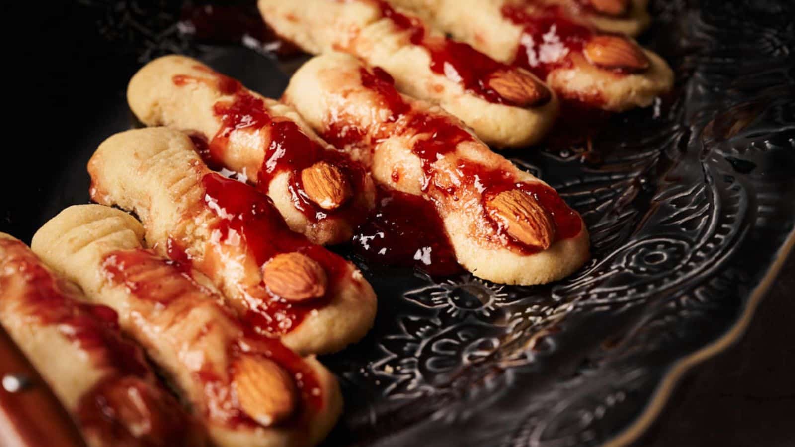 A plate of witch finger cookies with jam and jelly on it.