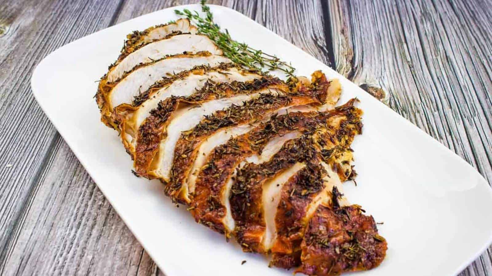 Sliced turkey breast on a white plate with sprigs of thyme.