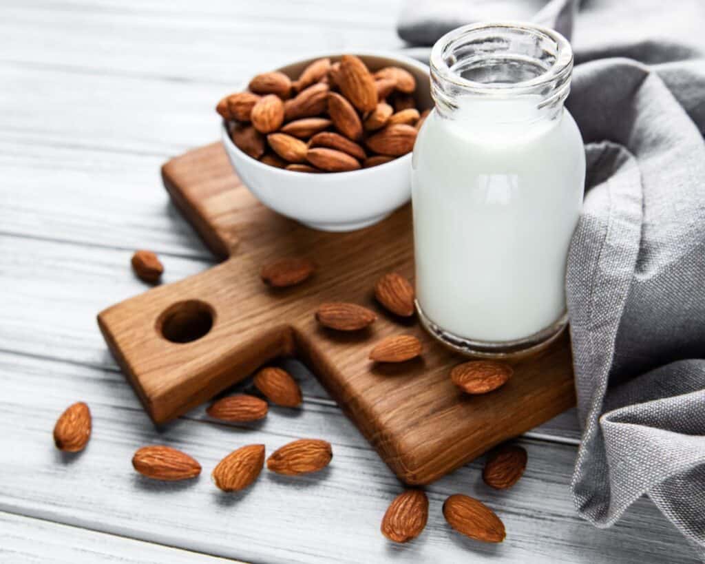 Almond milk and almonds on a wooden cutting board.