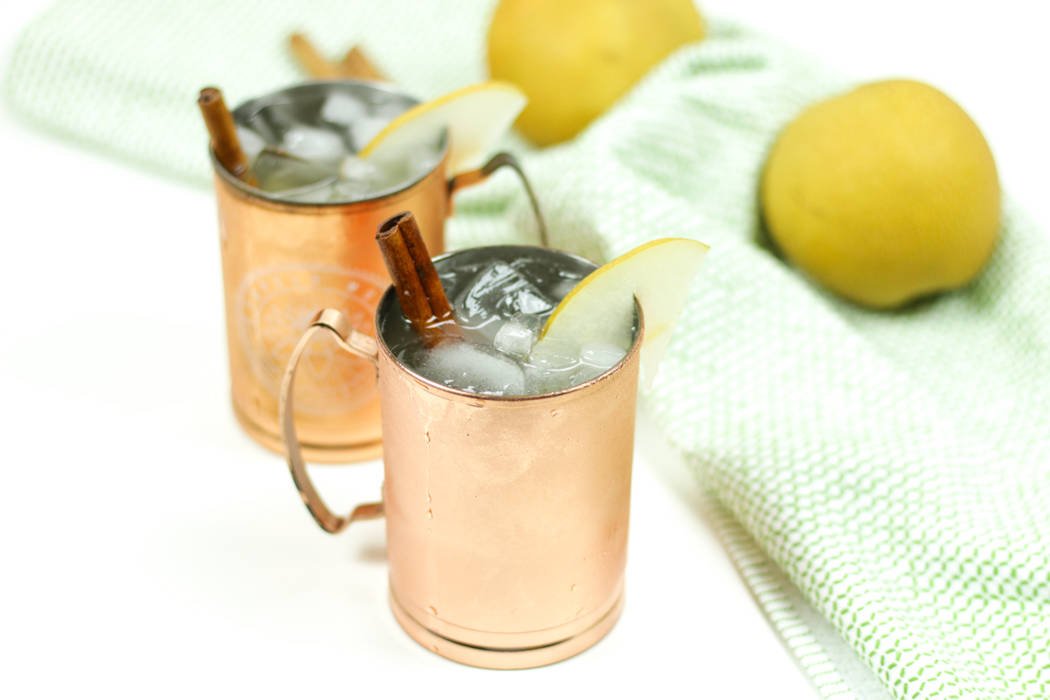 Two copper mugs with lemons and cinnamon, perfect for a refreshing pear moscow mule.