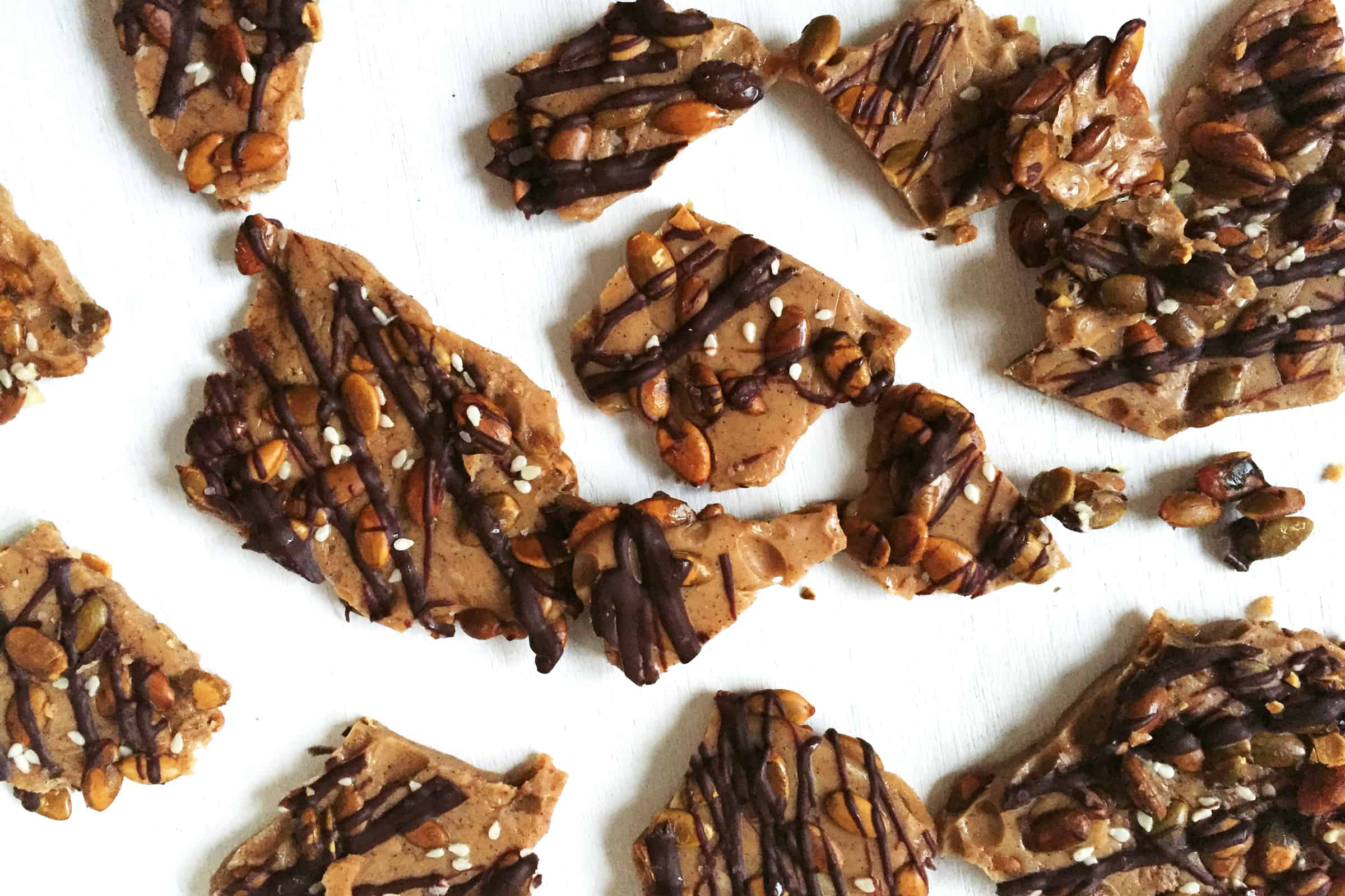 A plate of chocolate covered pumpkin brittle on a white surface.