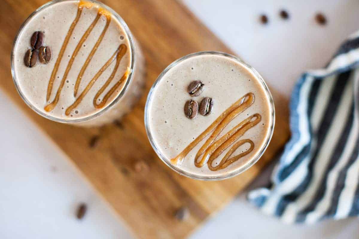 Two glasses of coffee and caramel smoothies on a wooden cutting board.