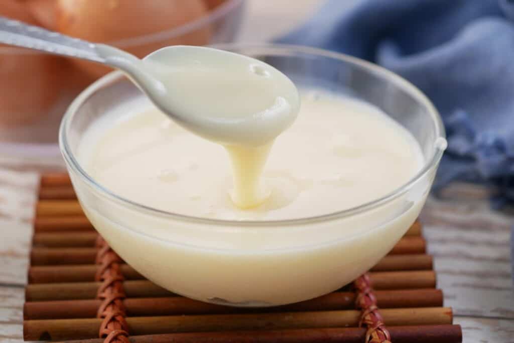A spoon of condensed milk is being poured into a bowl of condensed milk.