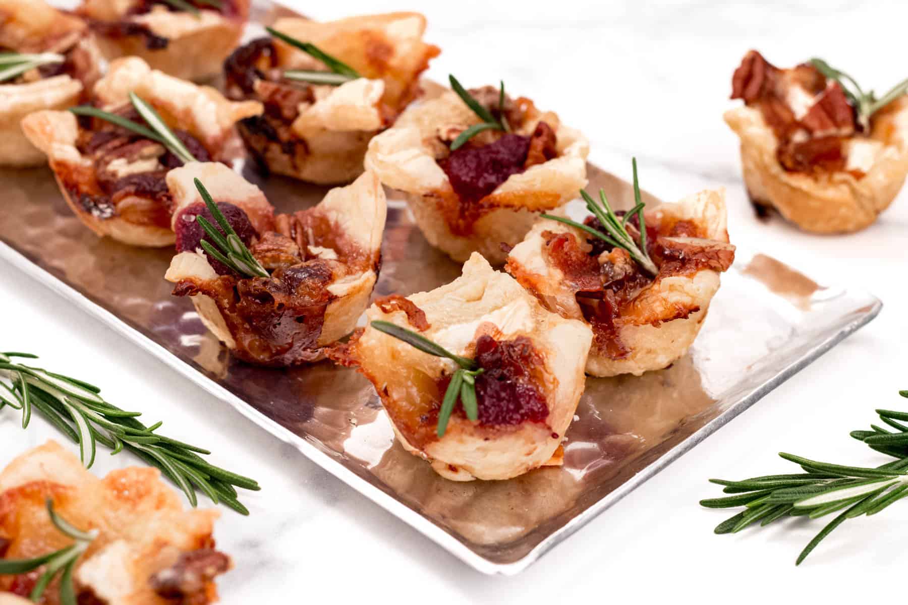 Appetizers with bacon and rosemary sprigs, perfect for Christmas recipes, served on a silver tray.