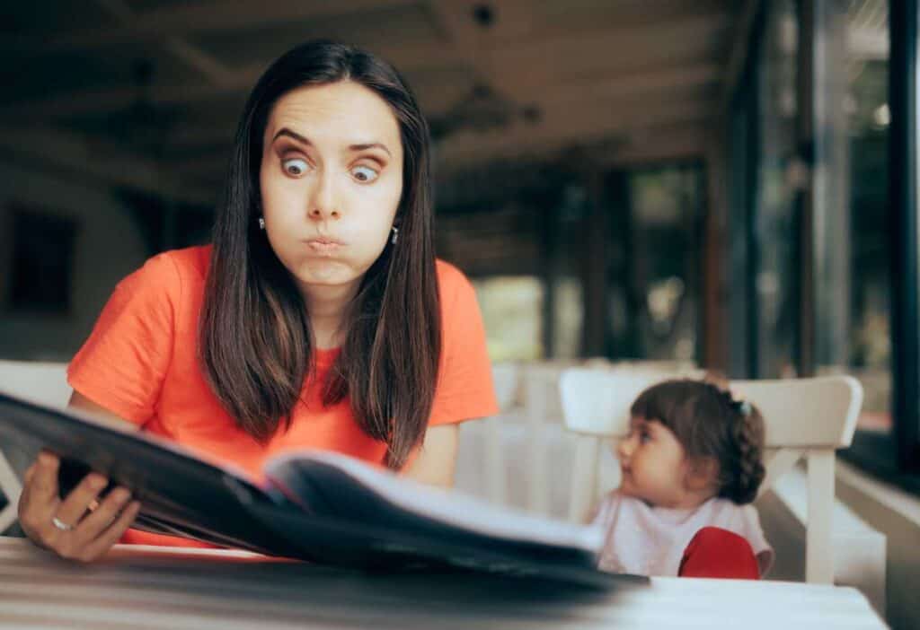 A woman is reading a menu while eating out with a child in front of her.