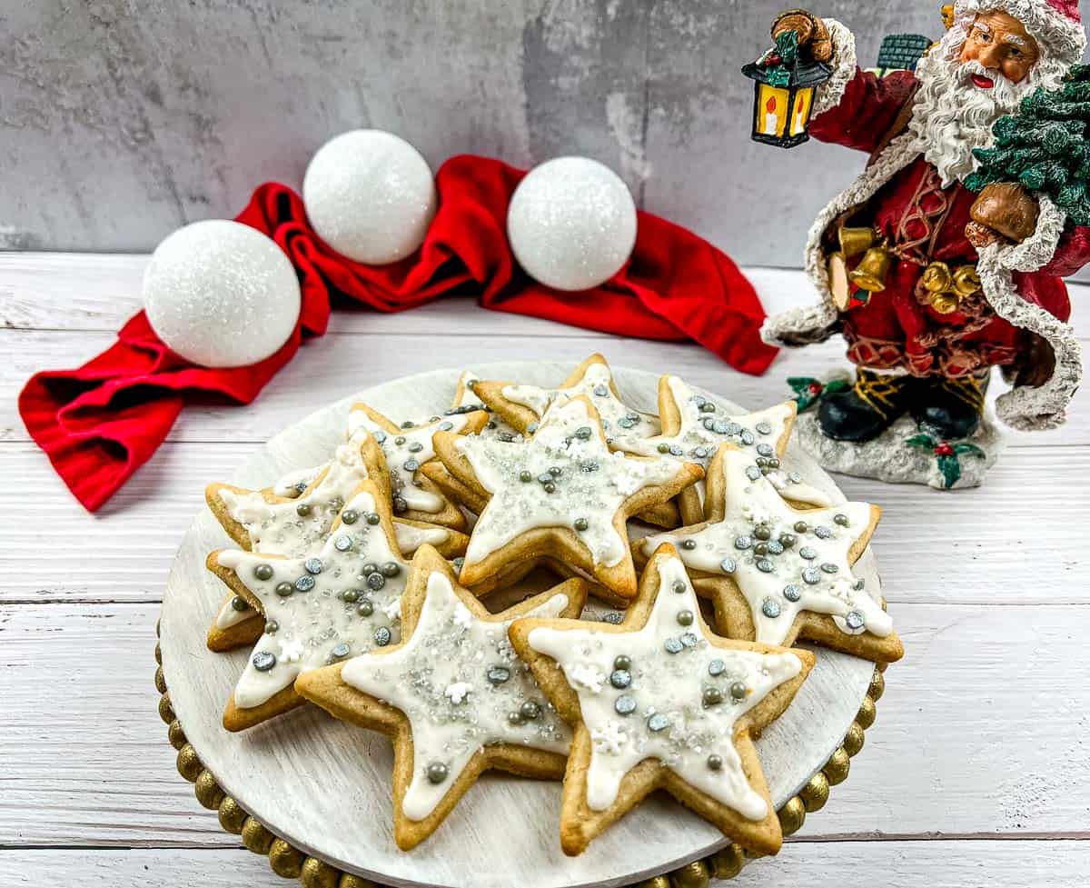 Eggnog sugar cookies on a plate with santa claus figurines.