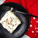 A piece of eggnog tres leches cake on a black plate with a fork.