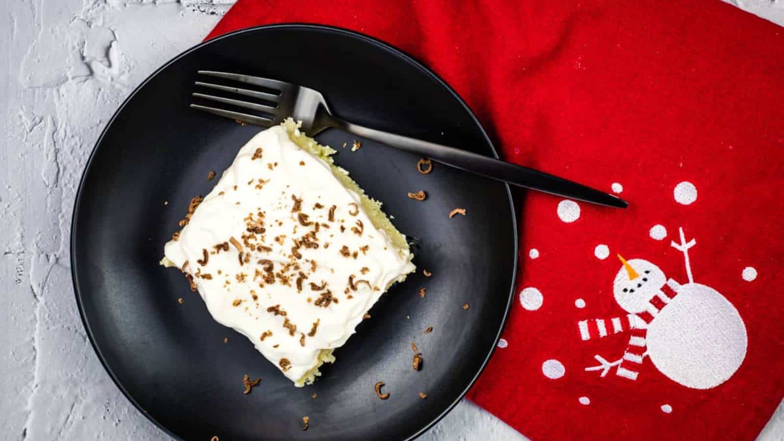 A piece of eggnog tres leches cake on a black plate with a fork.