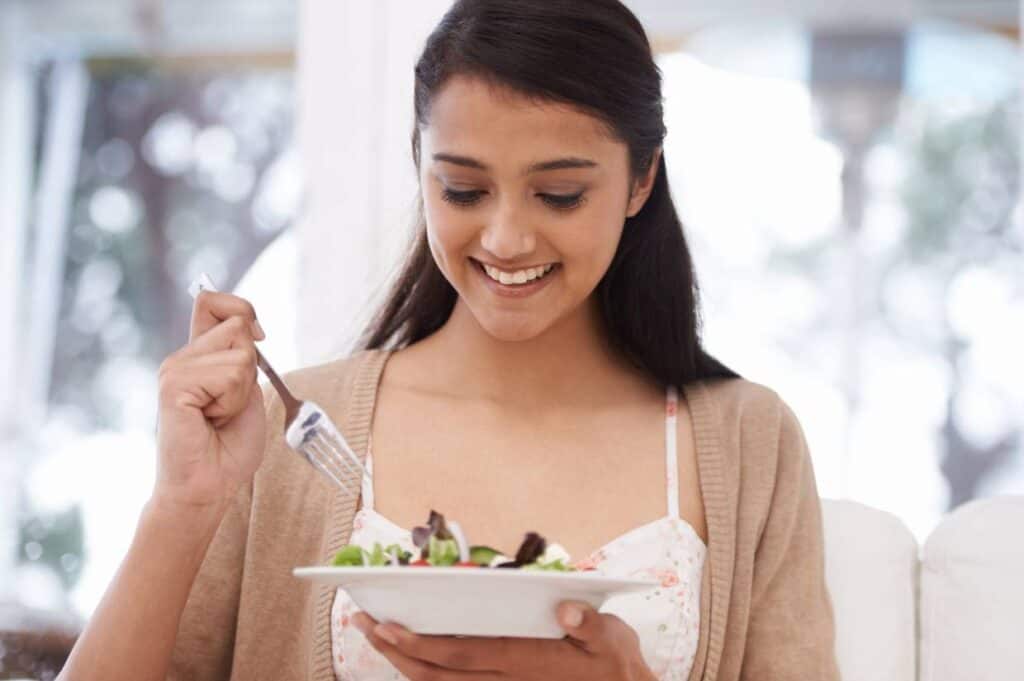 A woman is eating a salad with a fork as part of an elimination diet.