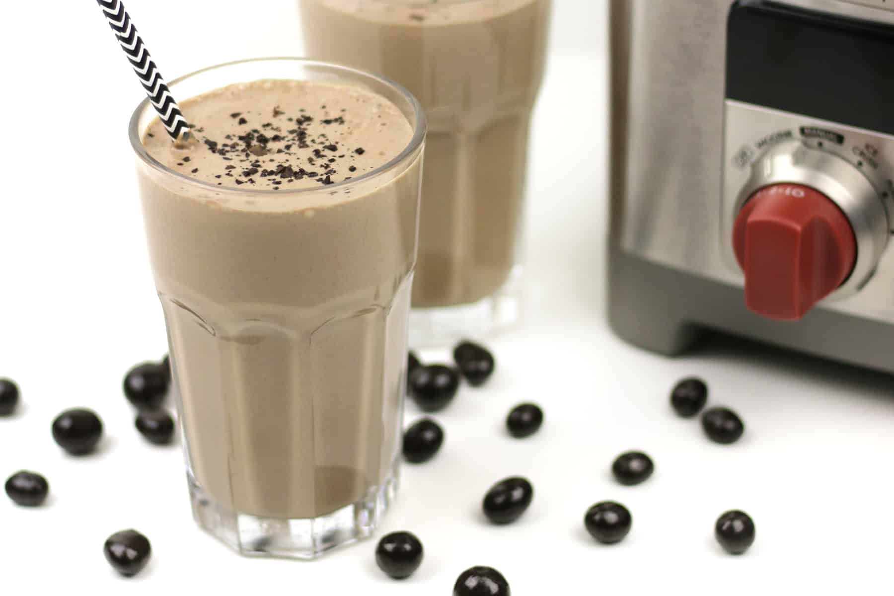 A blender with a cup of mocha smoothie and chocolate-covered espresso beans.