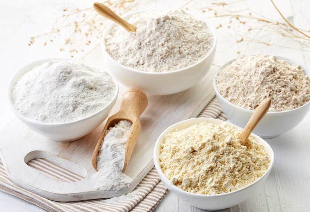 Various types of gluten free flours in bowls on a wooden table.