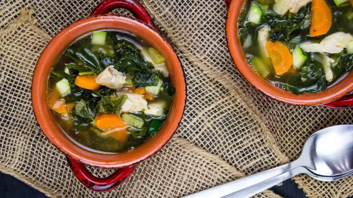 Two bowls of turkey and vegetable soup with spoons.