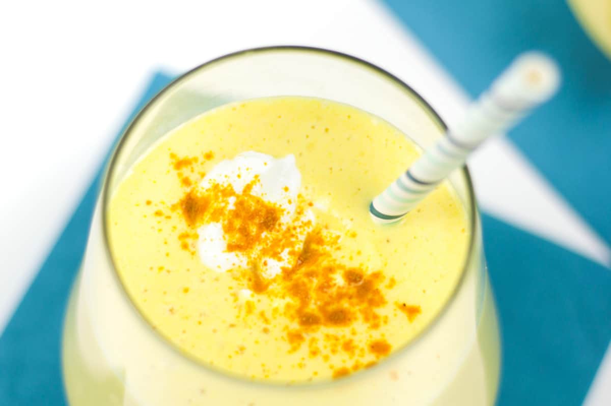 A glass of mango smoothie with yogurt and a straw.