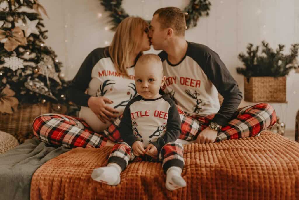 A family wearing matching Christmas PJs is sitting on a bed.