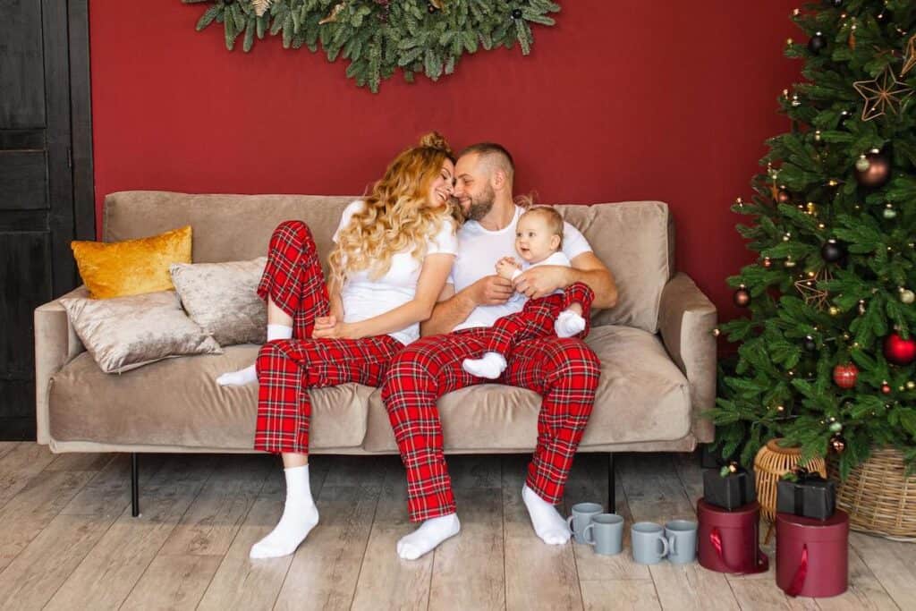 A couple in matching Christmas PJs sitting on a couch in front of a Christmas tree.