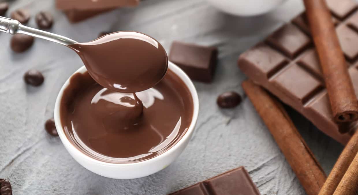 A spoon is pouring chocolate into a bowl with cinnamon sticks.