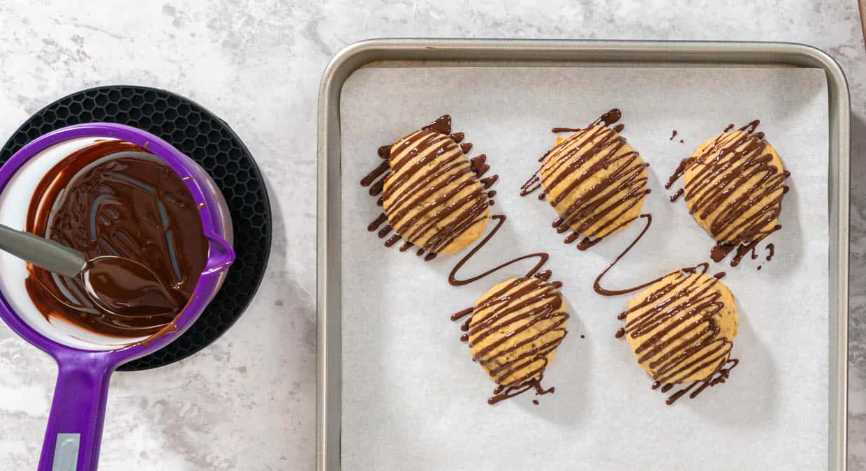 Chocolate dipped cookies on a baking sheet with a purple spatula.