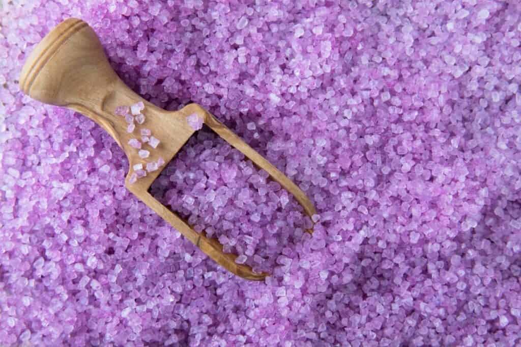 A wooden scoop is gently resting on top of purple bath salt.